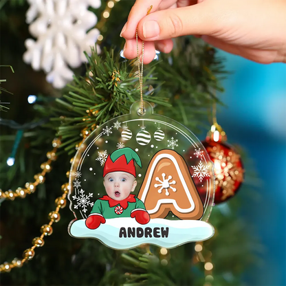 Christmas ornament with a child in an elf outfit and a gingerbread man, hanging on a tree.